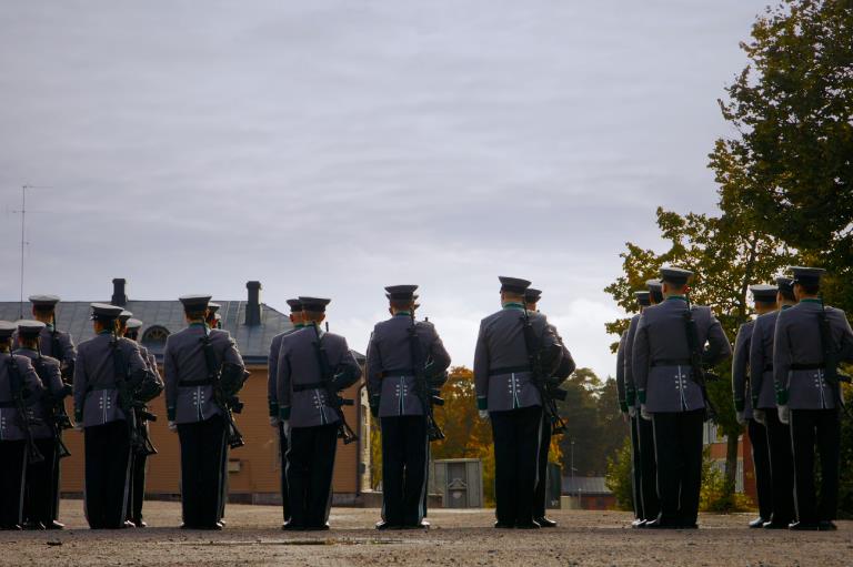 Sotilaat seisovat rivissä kasarmialueella selkä kameraan päin.