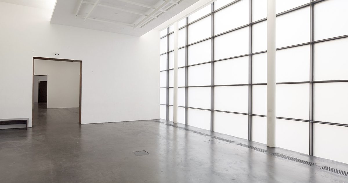 Huone, jossa on tumma lattia ja valkoiset seinät ja katto. Huoneen oikeanpuoleinen seinä koostuu lasista ja mustista alumiinikehyksistä. 