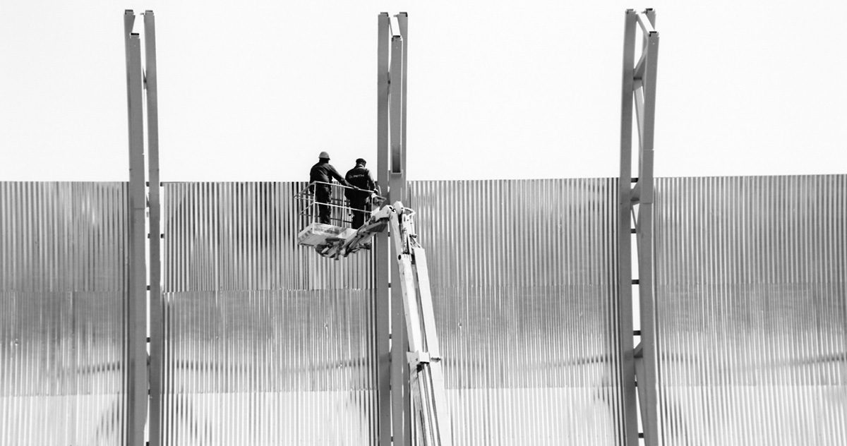 Rakennustyömaa, jossa kaksi miestä seisoo nosturin korissa.