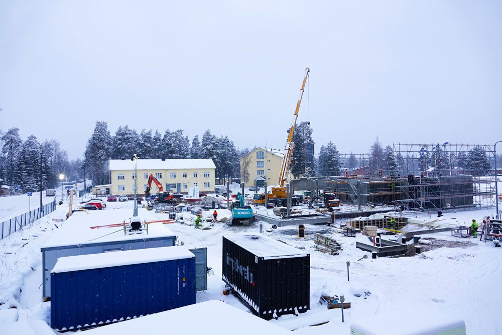 Talvisella työmaa-alueella nosturi, työmaatelineitä ja kontteja.