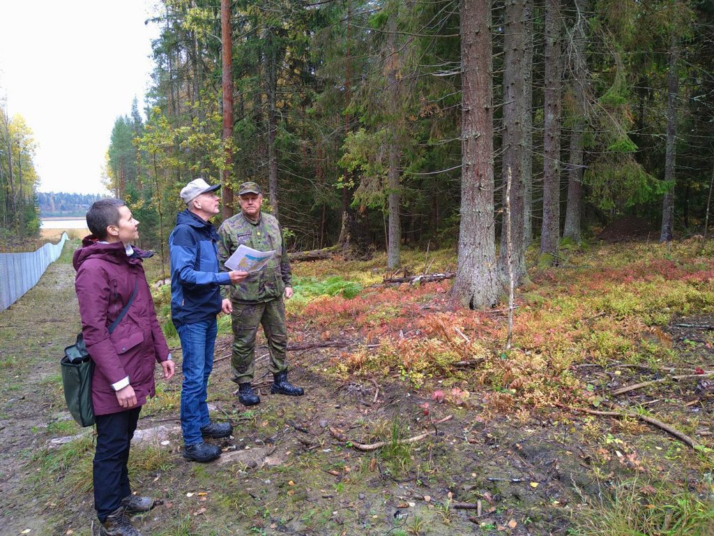 Kolme henkilöä on luontokävelyllä metsässä. Takana raja-aitaa.