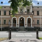 Vaalea arvorakennus, jonka sisäänkäynnissä kaarevat yksityiskohdat.