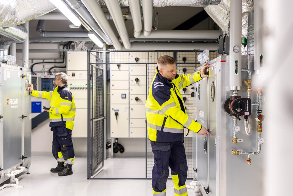Kaksi keltatakkista huoltomiestä säätää laitteistoja.