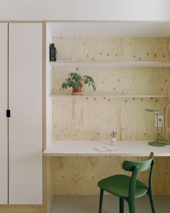 Puuseinä, johon on kiinnitetty puulevyjä. Edessä vihreä tuoli ja vasemmalla korkea kaappi.