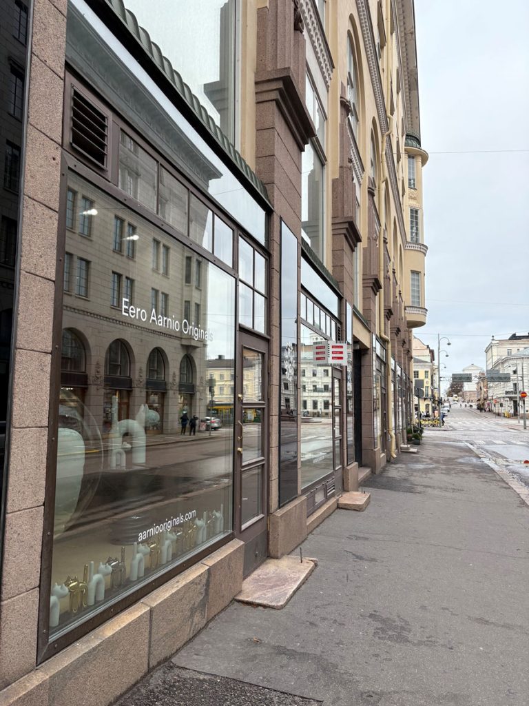 Katunäkymä jalkakäytävältä, jossa vasemmalla kivitalo ja sen näyteikkunoita.