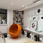 Liiketila takaseinän suuntaan. Seinät on maalattu valkoisella ja sinne on ripustettu esittelymateriaalia. Katossa näkyy valopisteet.