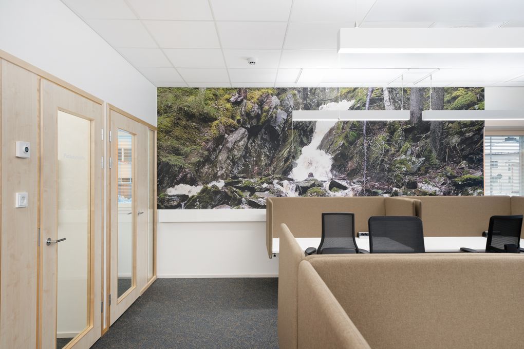 Tytila, jossa on työpöytiä, tuoleja ja luonnonaiheinen seinämaalaus vesiputouksesta.