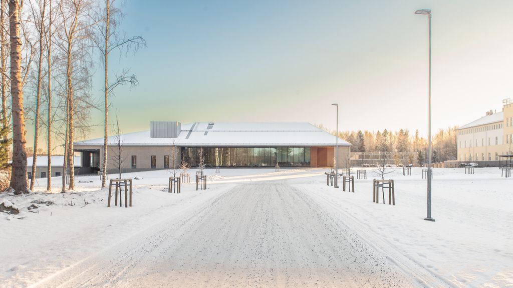 Lumipeitteinen tie johtaa modernille rakennukselle, jota ympäröivät talviset puut. Vaaleassa rakennuksessa laajasti ikkunaseiniä.