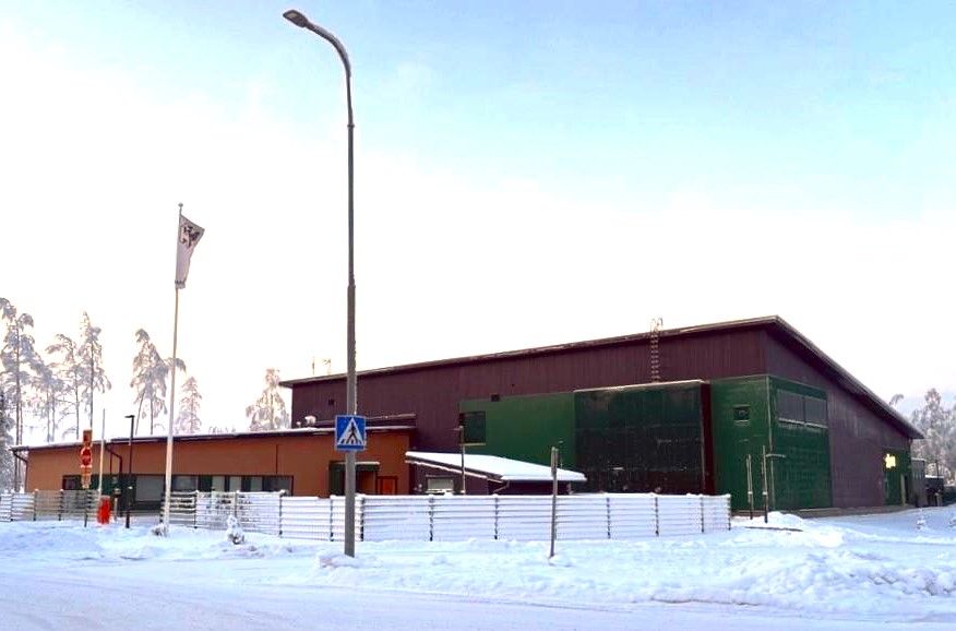 Luminen katu ja matala rakennus, taustalla talvinen metsä.