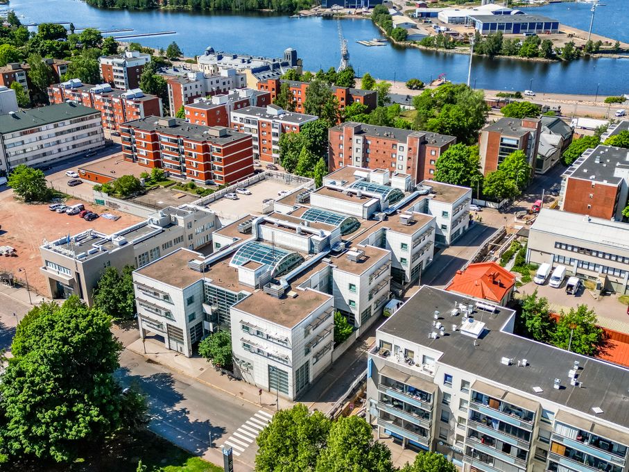 Ilmakuva urbaanista alueesta, jossa on tiiviisti sijoitettuja rakennuksia, puita ja vesistö taustalla.