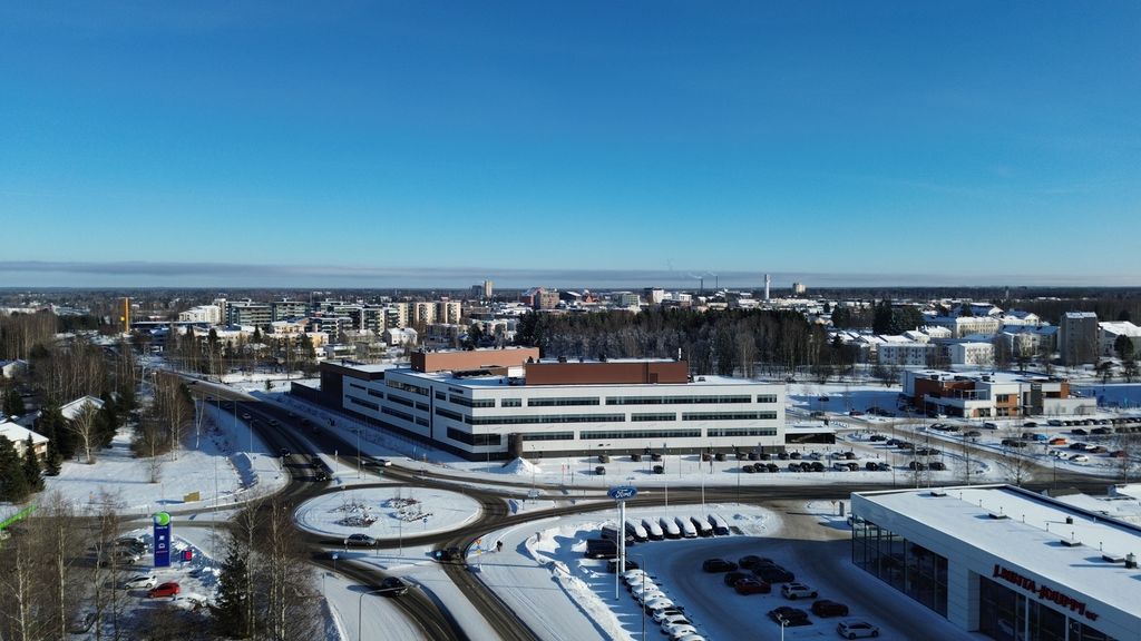 Ilmakuva valkoisesta monikerroksisesta rakennuksesta. Edessä liikenneympyrä ja pysäköintialueita lumisessa ympäristössä sekä taustalla kaupungin siluetti.