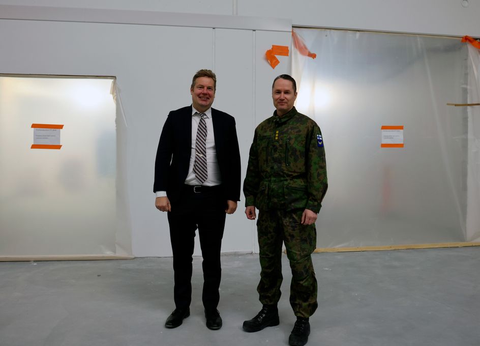 Tilaisuudessa Puolustuskiinteistöjen toimitusjohtaja Matias Warsta ja Karjalan lennoston komentaja eversti Tomi Böhm seisovat yhdessä hymyillen materiaaliterminaalin rakennustyömaalla.