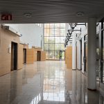 Rakennuksen läpileikkaava valoisa iso ala-aula. Valkoinen laatoitettu lattia ja päädyssä lattiasta kattoon ulottuva lasiseinä.