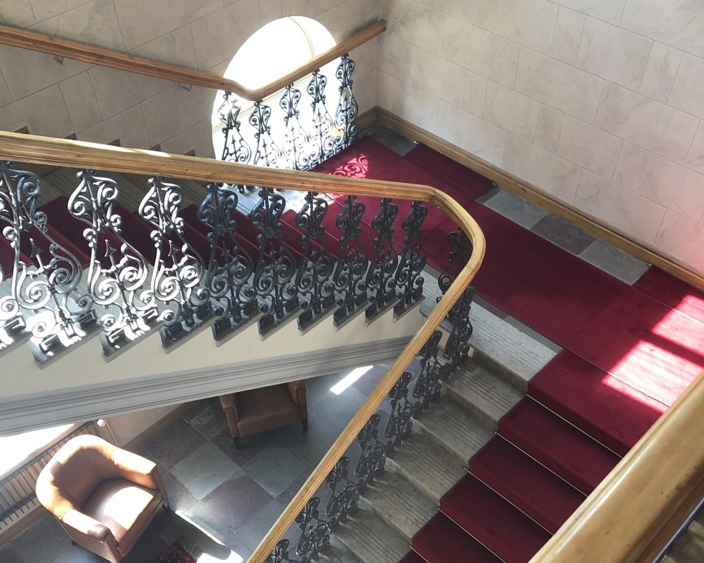 Oulun lääninhallituksen sisäportaikko, jossa koristeelliset kaiteet ja tummanpunaiset matot rappusissa.