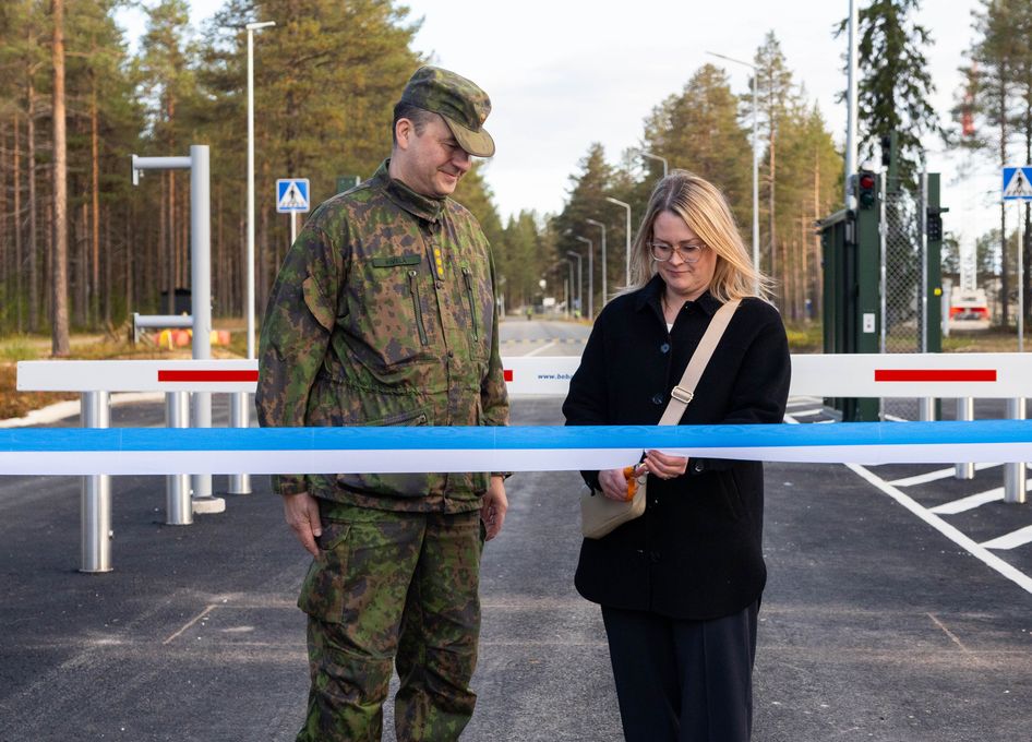 Nainen leikkaa sinisen nauhan virkapukuisen miehen vieressä.
