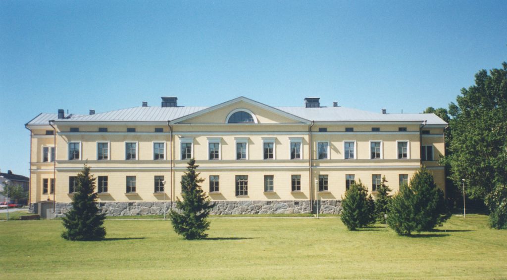 Keltainen, kaksikerroksinen historiallinen rakennus nurmikentän edessä.